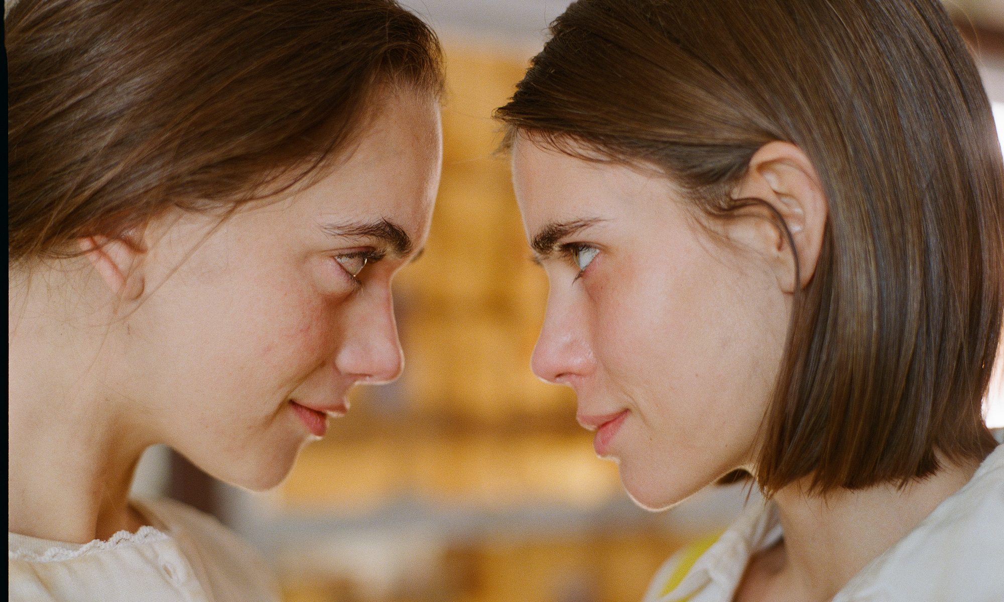 Herra and Bea, the two sisters, face each other at close range, almost touching.