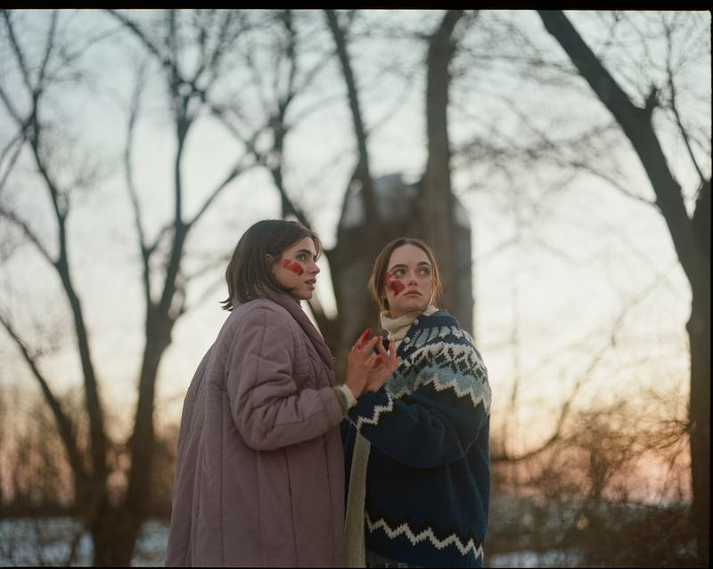 The sisters, in winter coats, among bare trees at dusk.