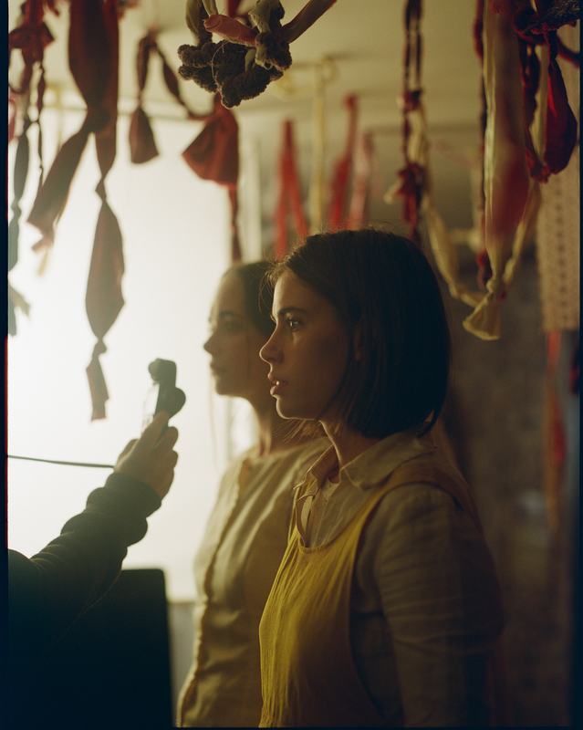 The sisters in profile, lit from a window, under hanging cloth.