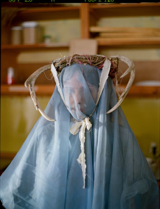 A ceremonial figure draped in a pale blue veil, crowned with antlers.