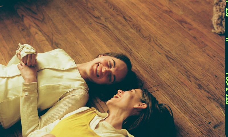 The sisters lie on a wooden floor, laughing.